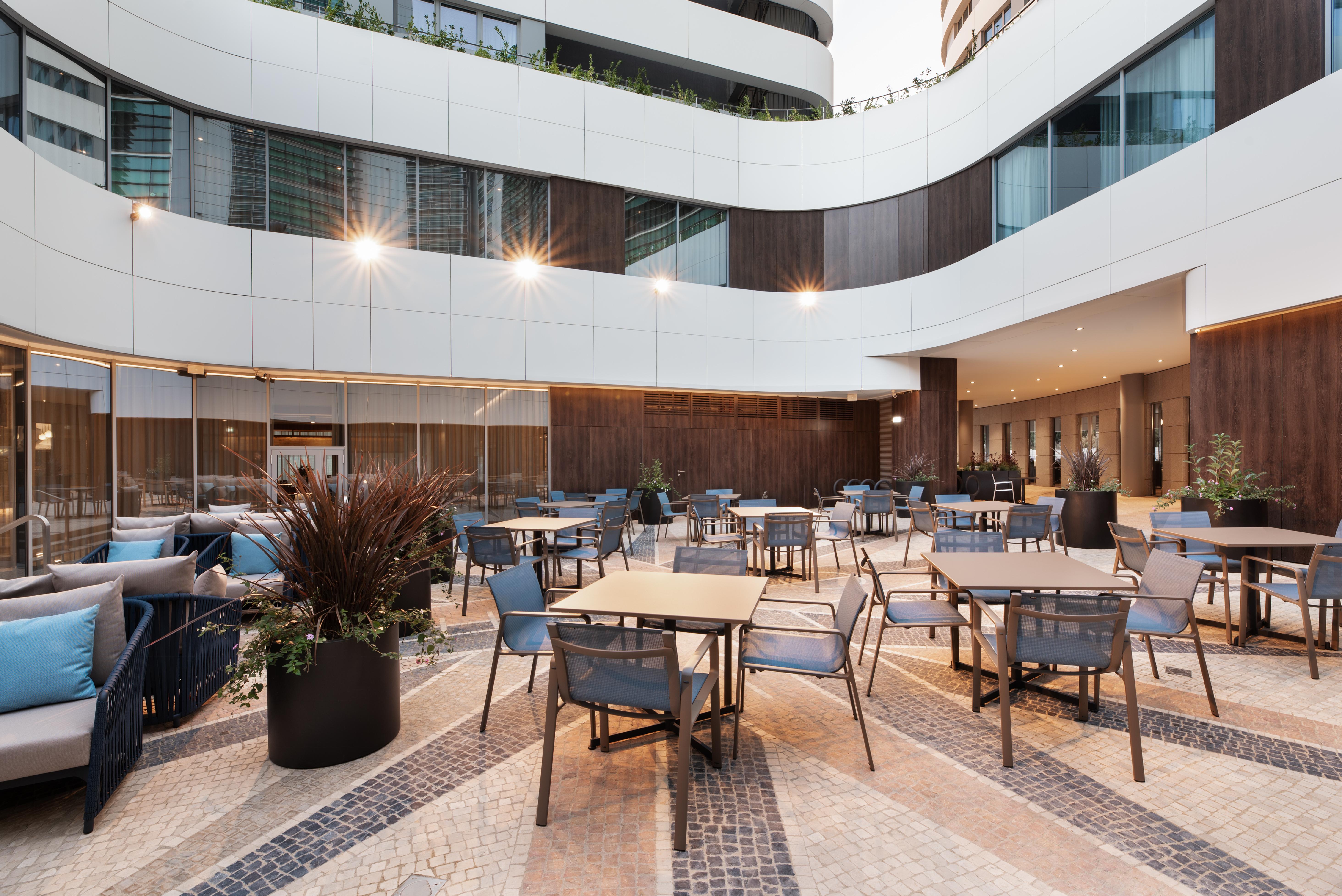 Eurostars Universal Lisboa Hotel Exterior photo The photo depicts a modern outdoor dining area in an architectural setting. It features multiple tables and chairs arranged in a spacious layout. The floor is designed with a combination of tiles and stone patterns, creating an attractive visual appe